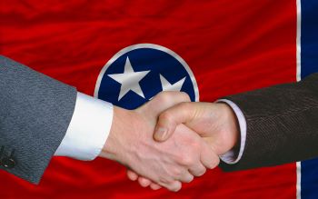 two businessmen shaking hands after good business investment agreement in front US state flag of tennessee