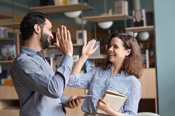 ly professionals giving high five standing in office celebrating success.