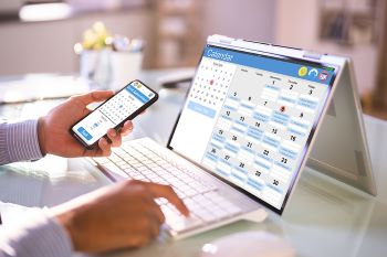 Closeup photo of person looking at month agenda on both laptop and mobile calendar