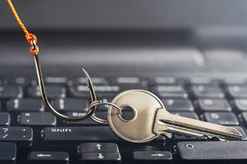 A photo of a fish hook dragging a key by its ring across the surface of a computer keyboard to portray the idea of online theft.