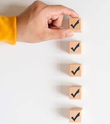 A hand is reaching in to adjust one of five wooden cubes with checkmarks printed on them.