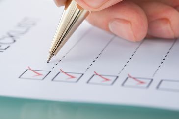 Close up image of a person's hand holding a pen and preparing a checklist